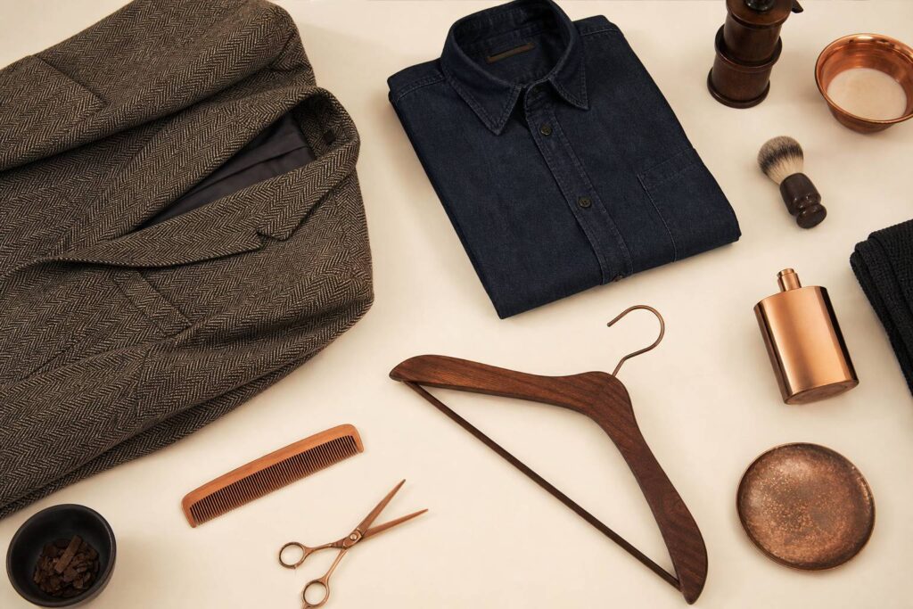 Flat-lay de mode avec veste en tweed, chemise en denim pliée et accessoires en cuivre sur fond crème